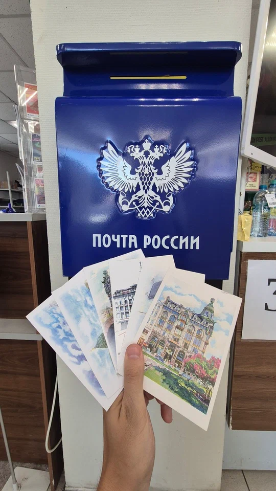 Открытки в руке возле синего почтового ящика